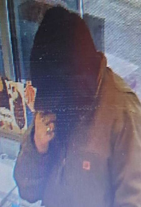 A man in a beige jacket with a hat and hood on. Only his hand is visible. 